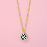 A gold toned necklace on a delicate chain with checkerboard inlay with mother of pearl and glass