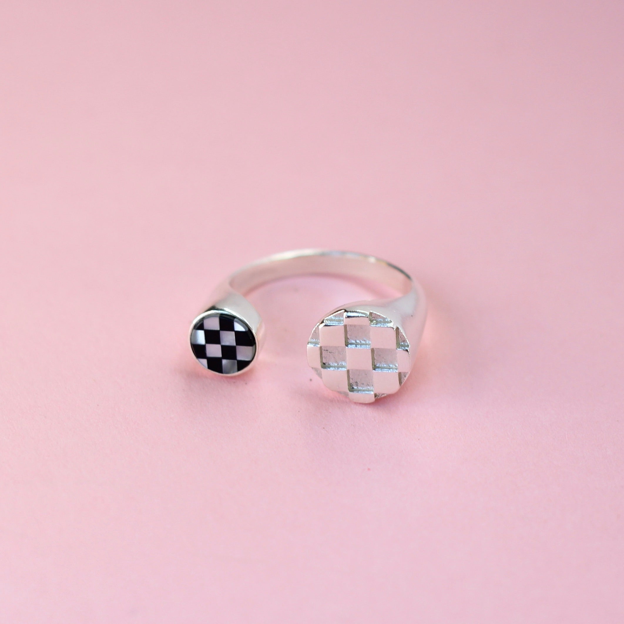 A silver split shank ring with a silver metal checkerboard pattern on on side and a mother of pearl and black glass inlay pattern on the other