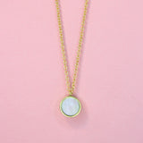 A close up of a gold toned bronze necklace with a circle iridescent mother of pearl charm