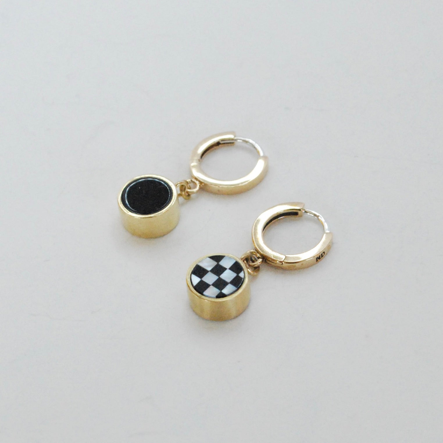A pair of gold-colored huggie hoop earrings with black and white checkered inlay charms and black onyx on a white background.