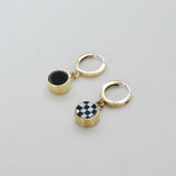 A pair of gold-colored huggie hoop earrings with black and white checkered inlay charms and black onyx on a white background.