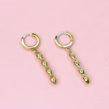 A pair of gold-colored huggie hoop earrings with dangling sculptural details on a pink background