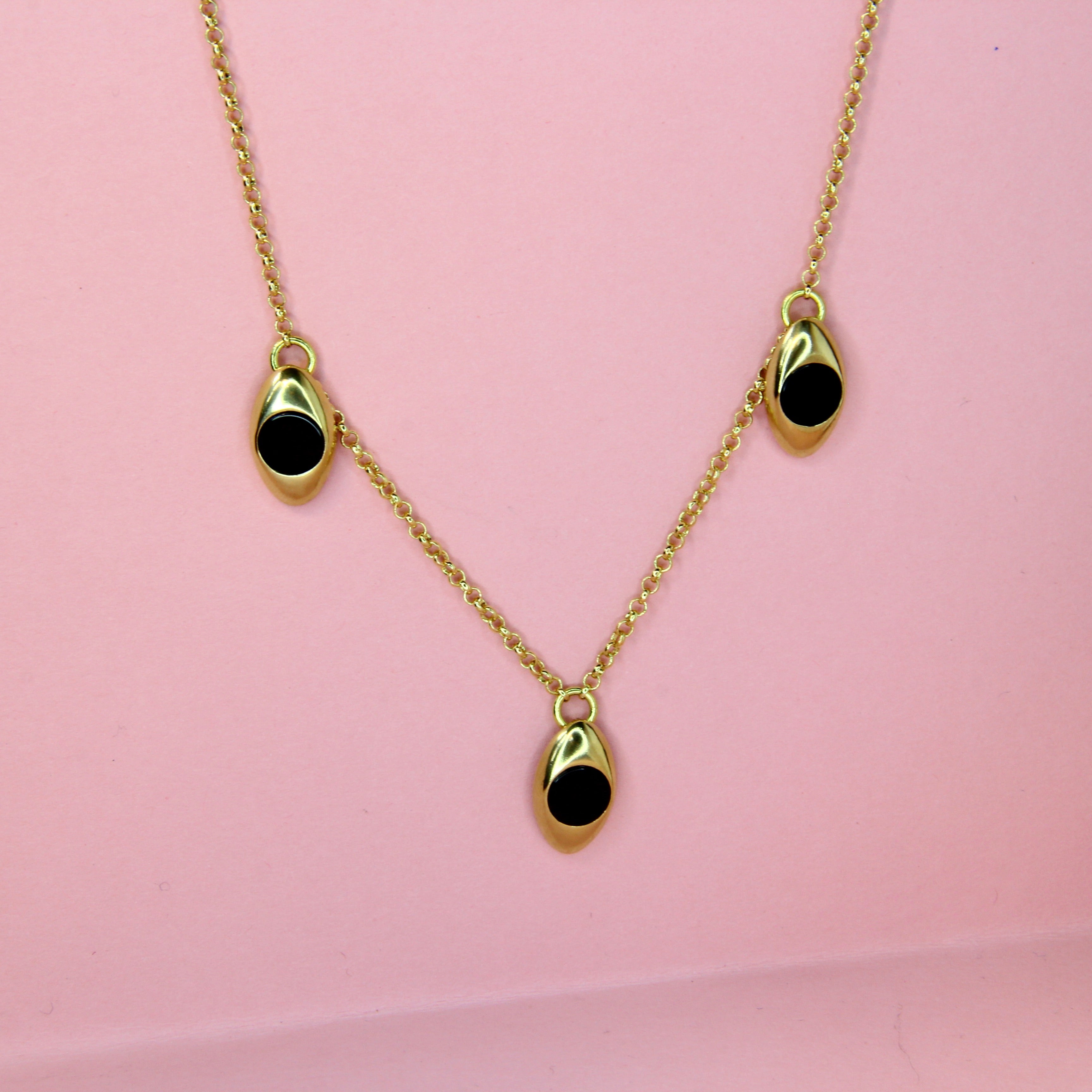 Bronze gold toned necklace with three black onyx inlaid stone charms on a pink background