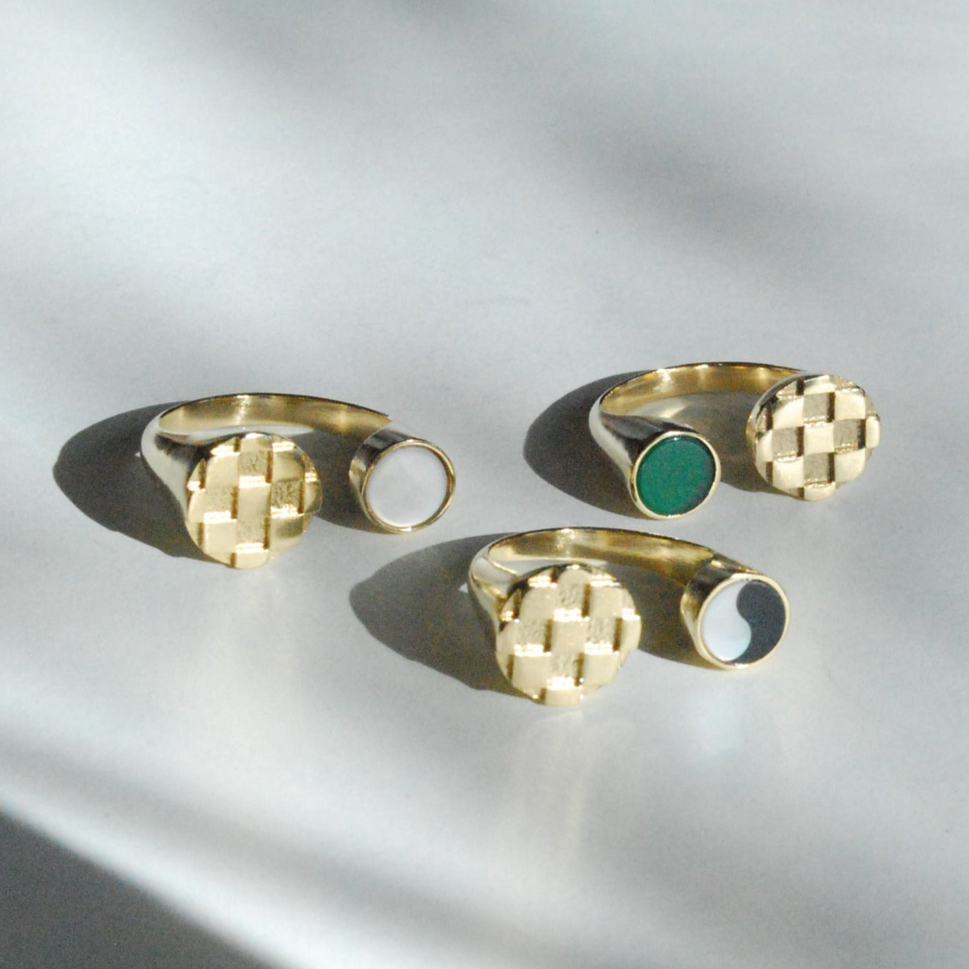 A collection of gold-colored split checkerboard inlay rings with different colored stones on a light surface.