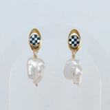 A pair of oval inlay pearl posts with baroque pearl dangles, with the earrings displayed in a gold-colored oval post and a checkered pattern on the inlay.