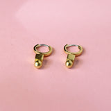 Bronze Huggie hoops with a geometric charm on a pink background