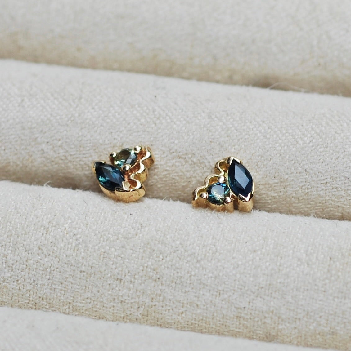 Pair of gold earrings with blue Australian sapphire gemstones on a beige fabric background