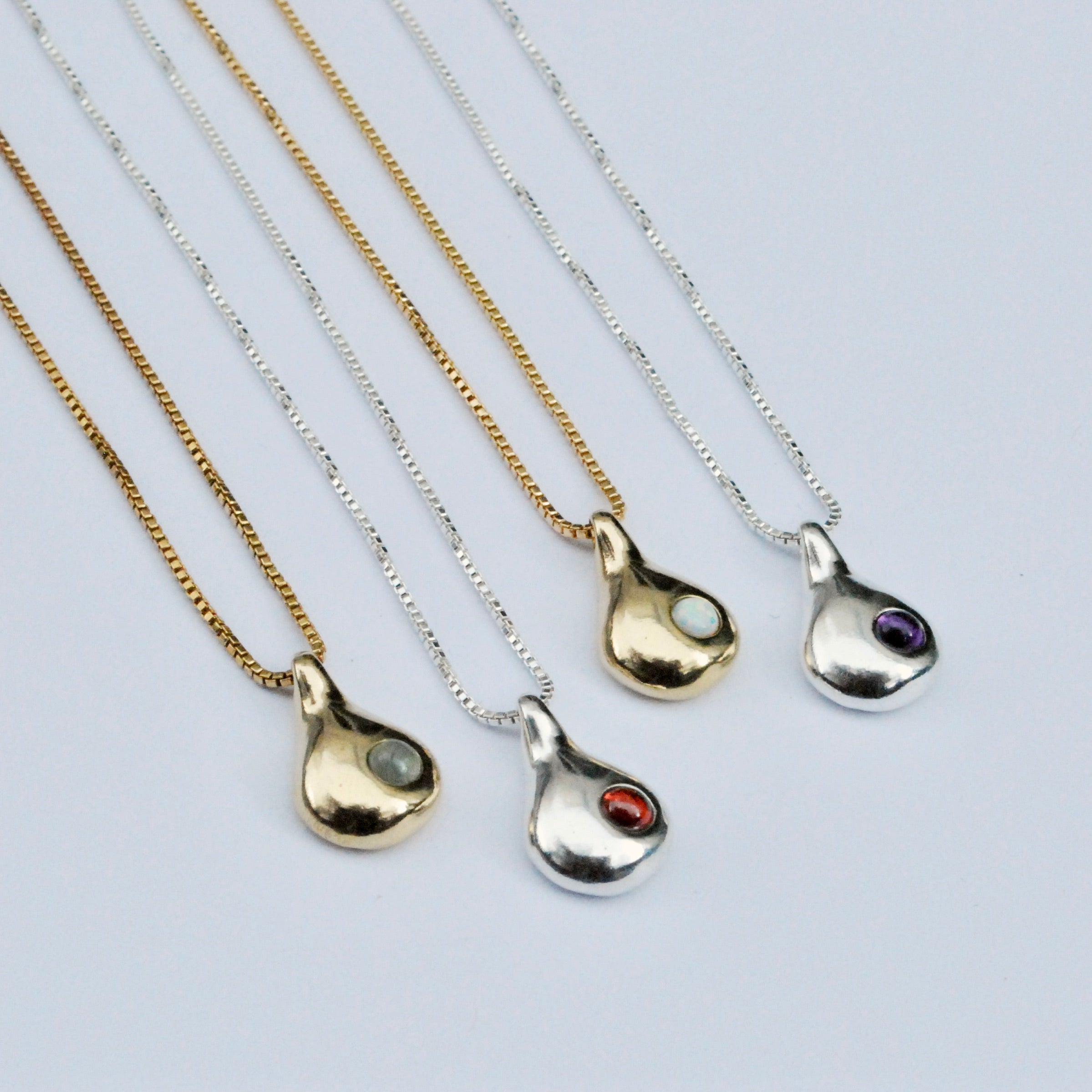 A collection of pendant necklaces with teardrop-shaped pendants in silver and gold colors, each featuring a different colored accent inside the pendant.