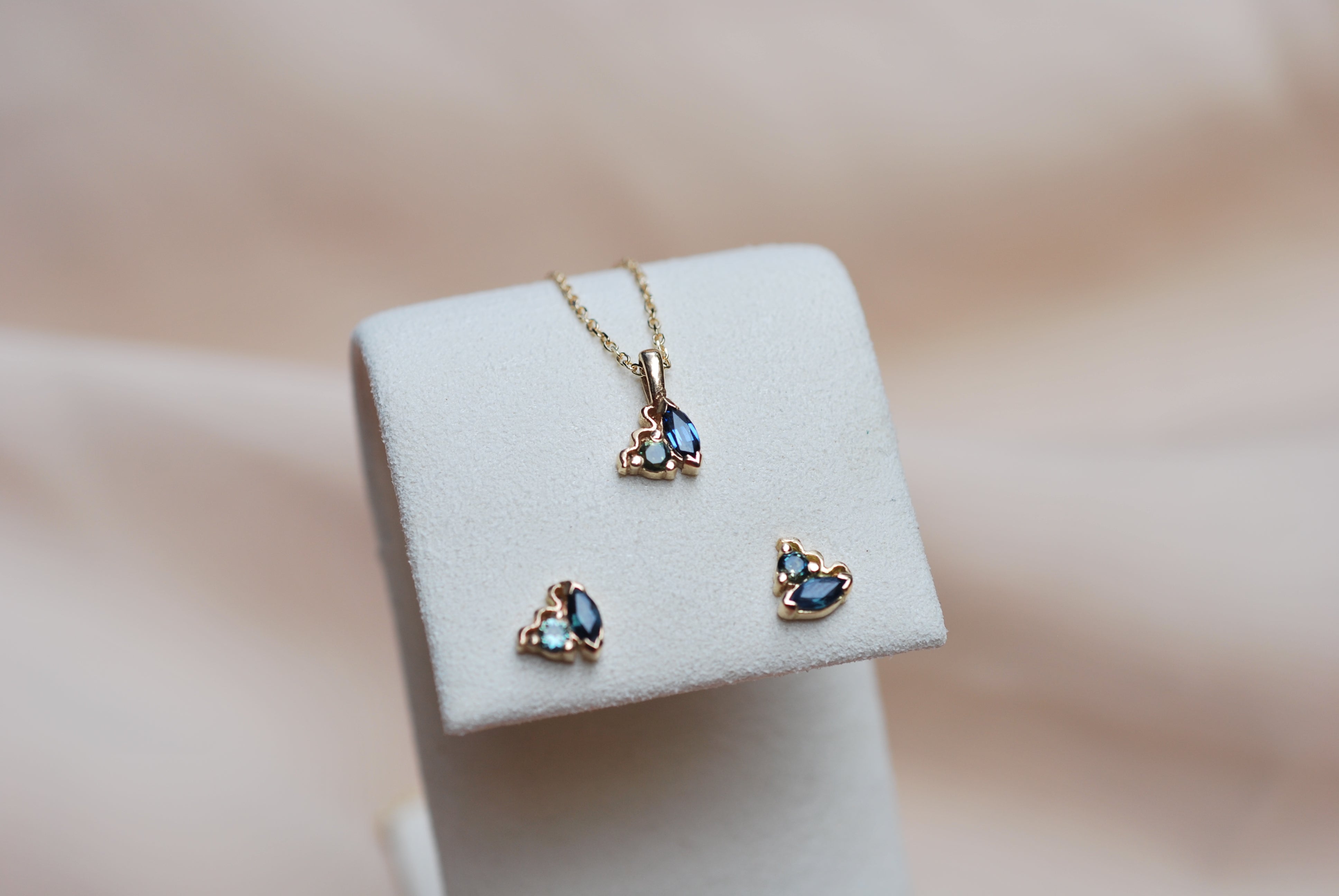 Gold necklace and earrings with blue gemstones on a white stand against a blurred background