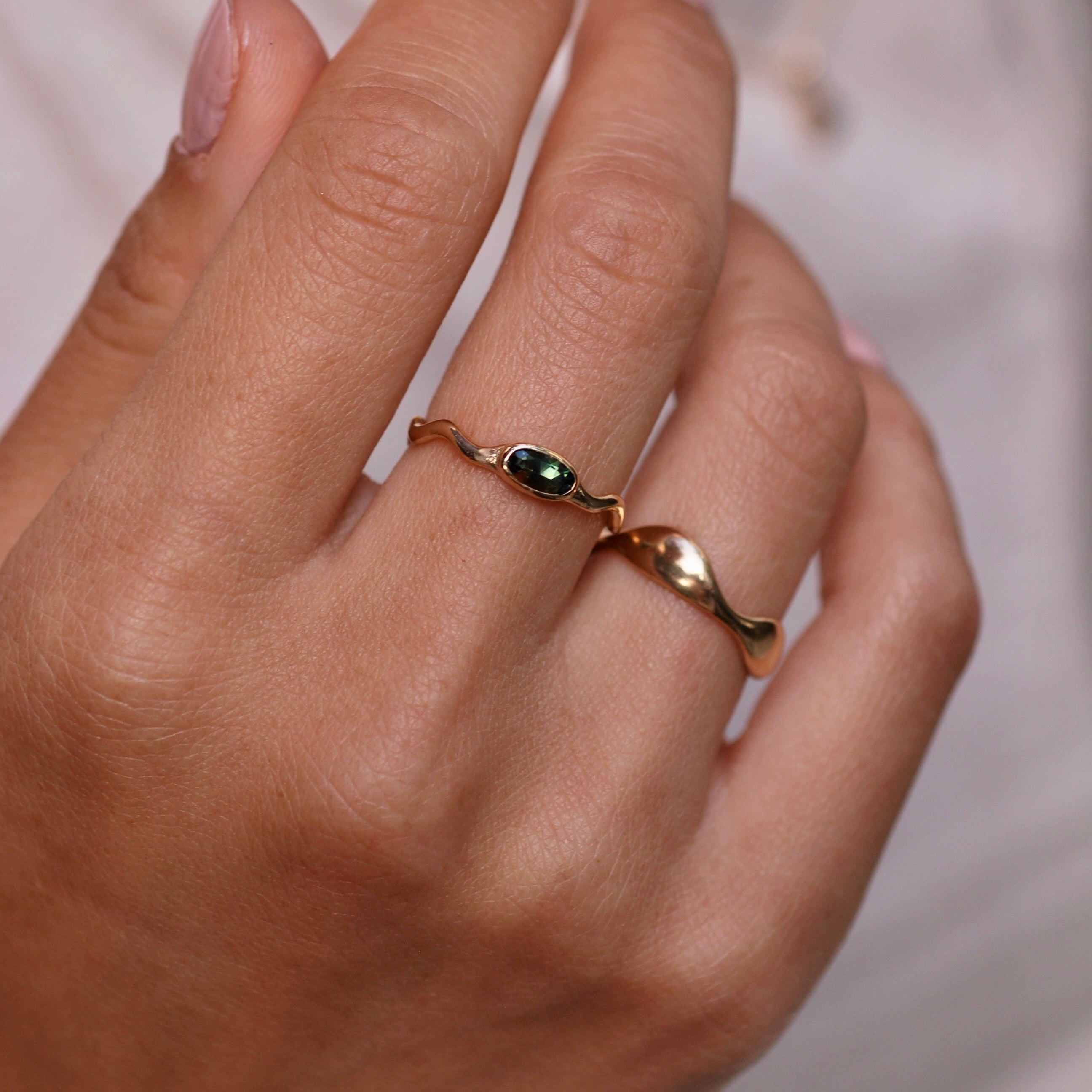 Close-up of a hand wearing a gold ring with a green gemstone on a blurred background