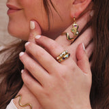 Close-up of a person wearing gold jewelry including earrings, rings, and a bracelet.