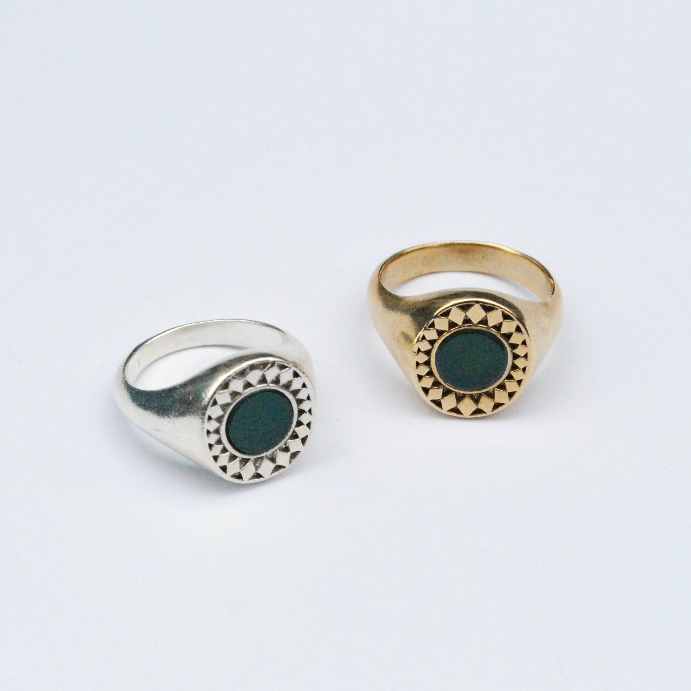 Two rings on a grey background, one silver and one bronze, both with green chrysoprase inlay stone surrounded by a star burst pattern