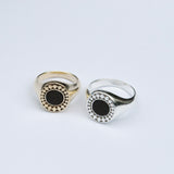 Two rings on a grey background, one silver and one bronze, both with a black onyx inlay stone surrounded by a star burst pattern