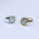 Two rings on a grey background, one silver and one bronze, both with a white mother of pearl inlay stone surrounded by a star burst pattern