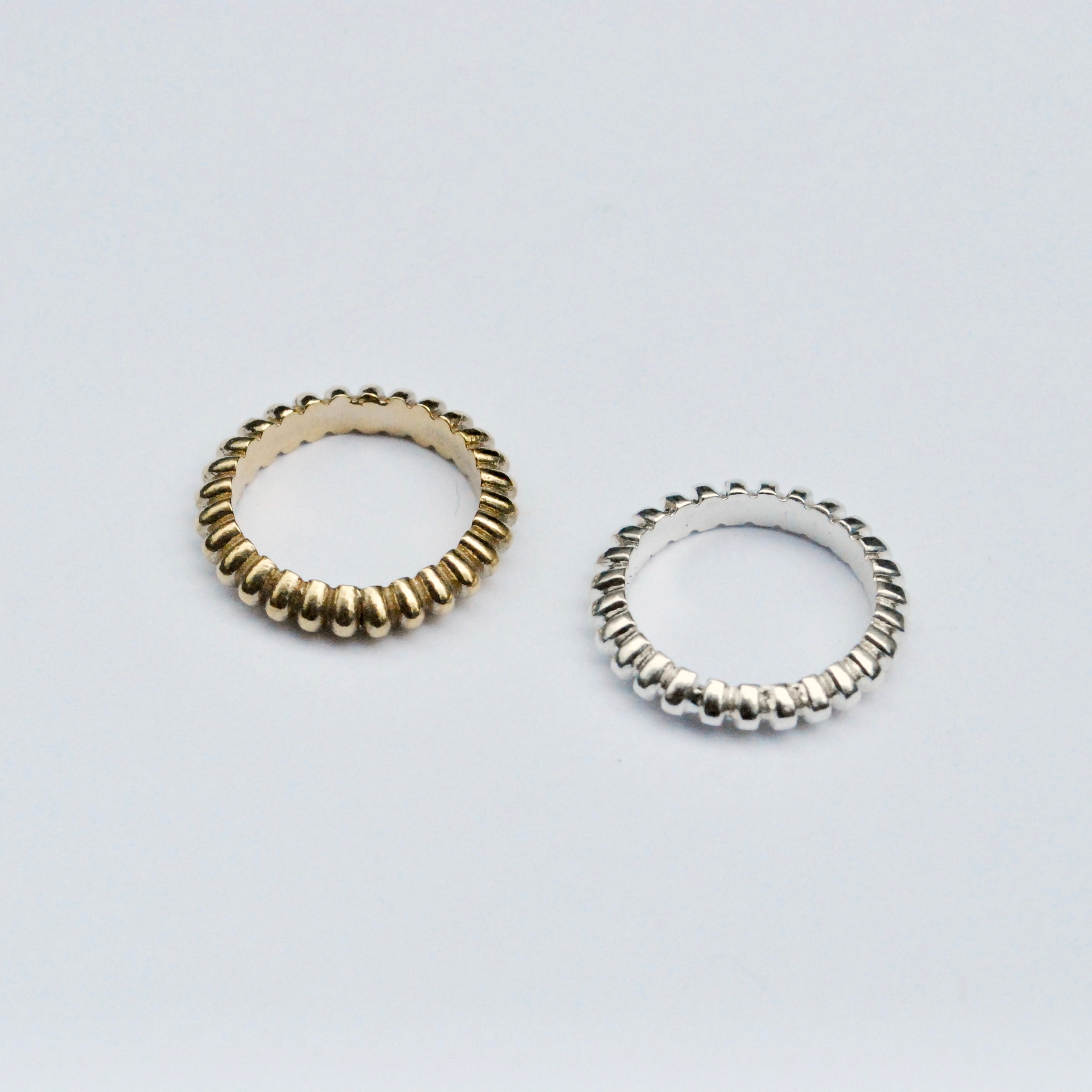 Two rings, one gold-colored and one silver-colored, with a textured, ridged design, displayed against a white background.
