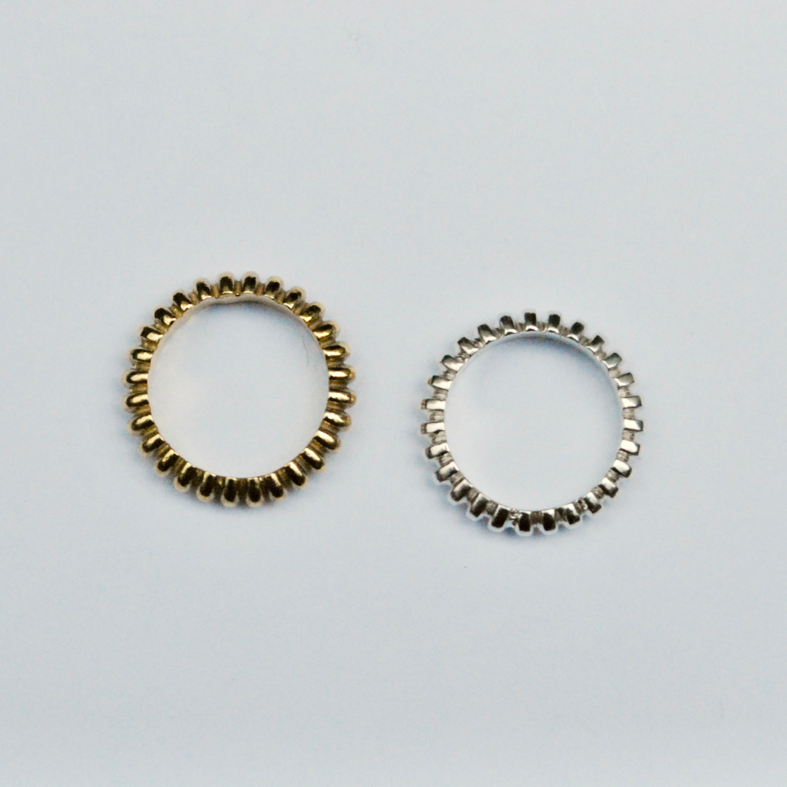 Two ring bands on a grey background, one silver and the other bronze with a repeated geometric pattern