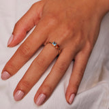 Hand wearing a gold ring with a blue square gemstone and a orange circle gemstone on a white background