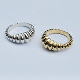 Two rings, one silver and one bronze with a ridged geometric pattern similar to a croissant on a grey background