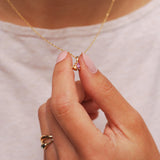 Hand holding a gold necklace with a pink and orange sapphire pendant against a neutral background