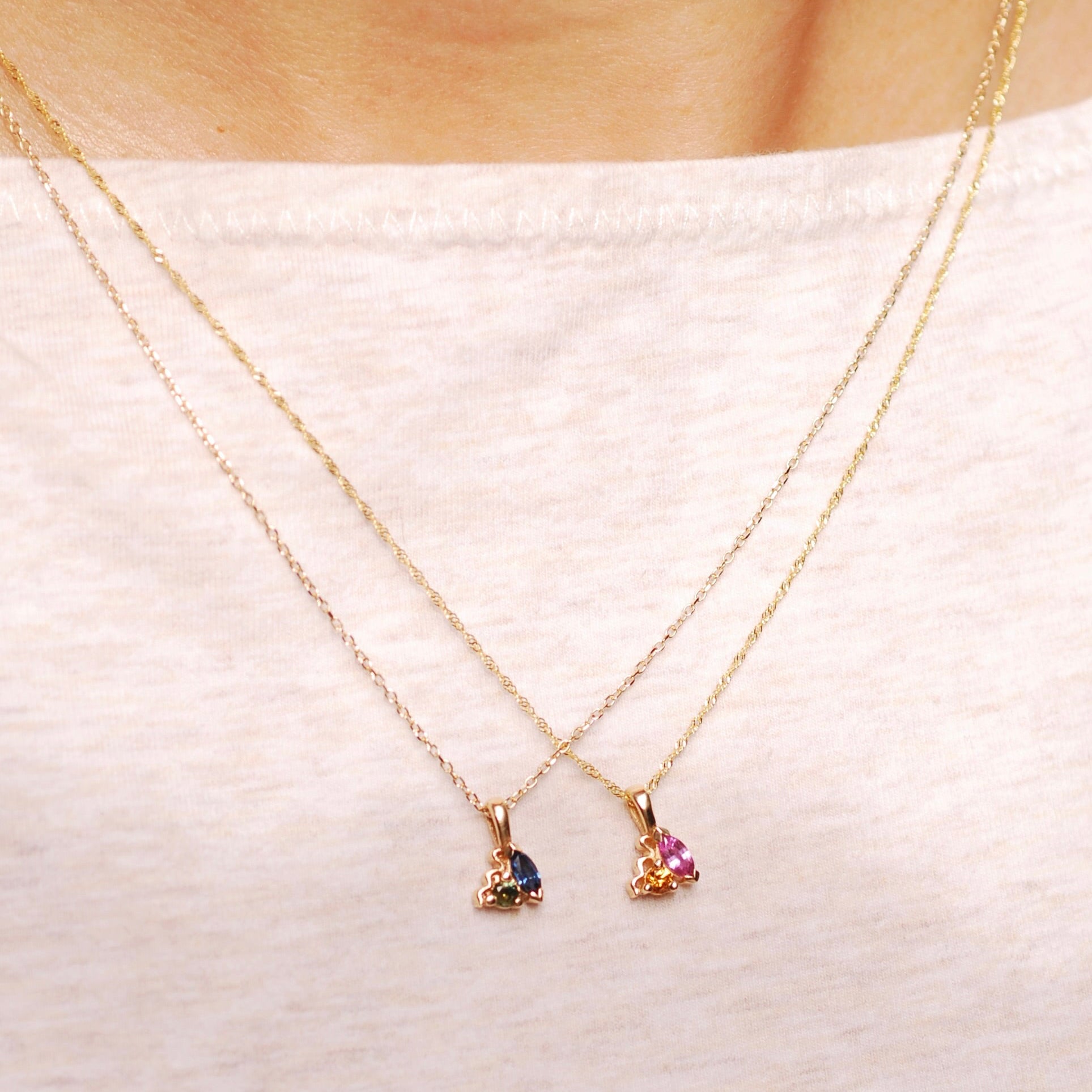 Two gold necklaces with gemstone pendants on a white fabric background
