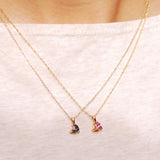 Two gold necklaces with gemstone pendants on a white fabric background