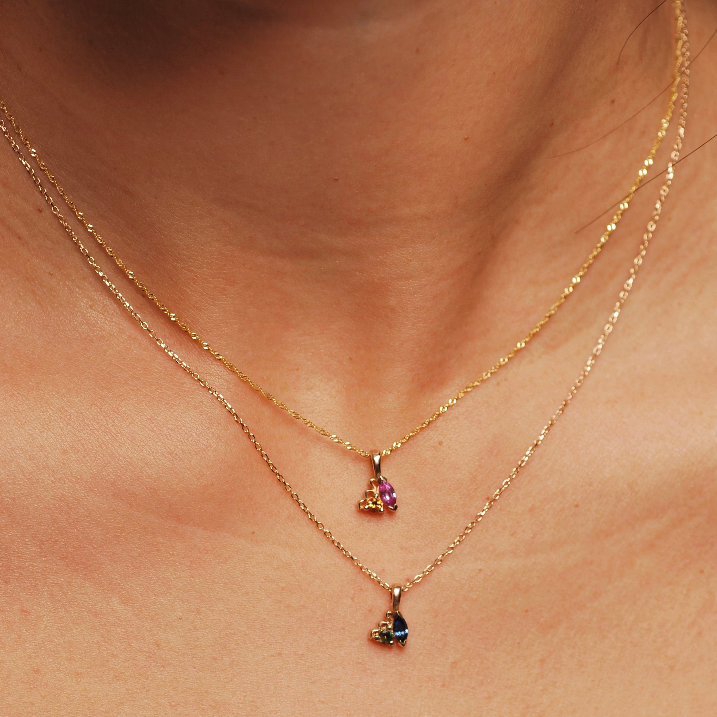 Two gold necklaces with cluster stone pendants on a person's neck.