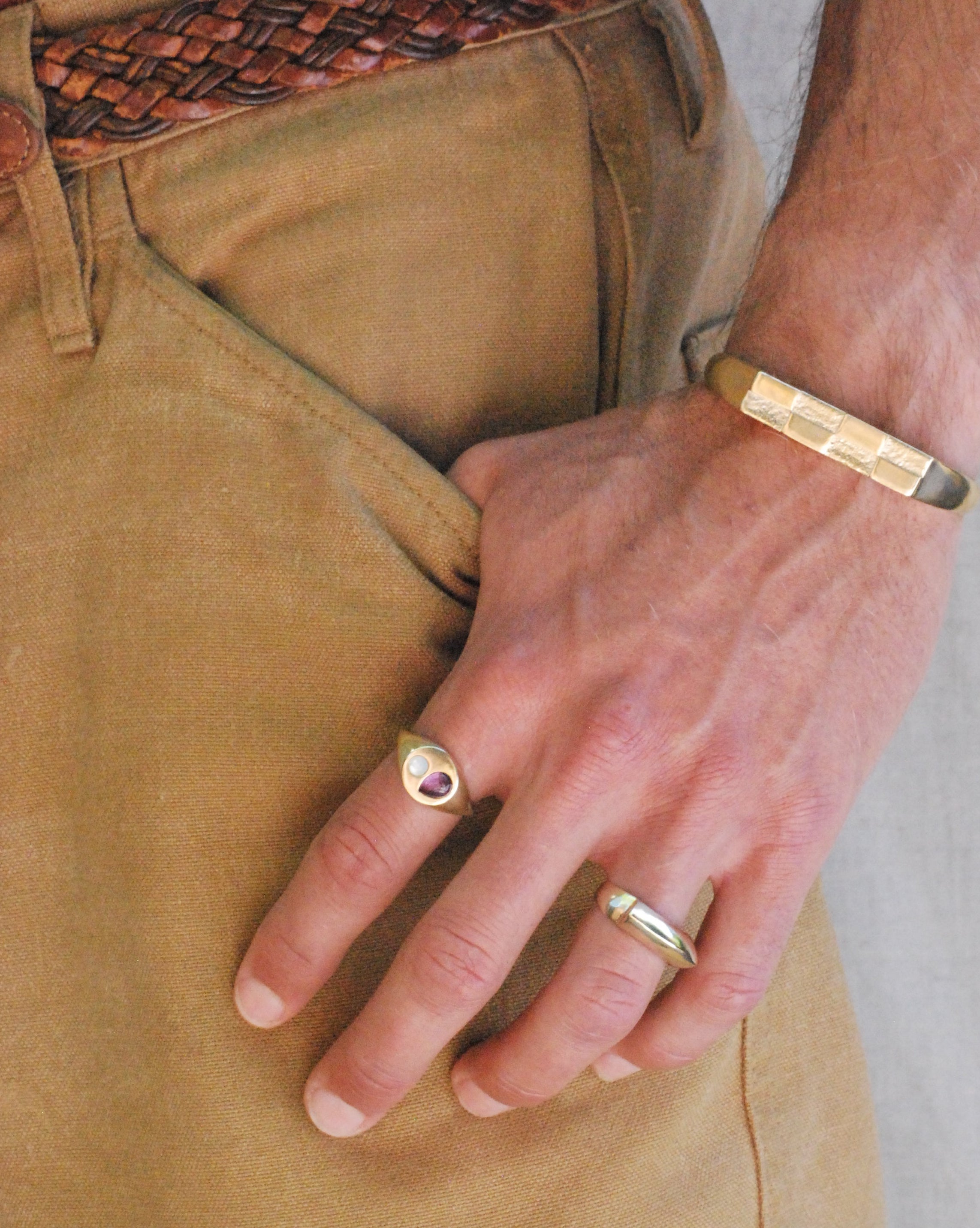 Hand wearing a gold ring and bracelet on beige pants.