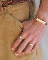 Hand wearing a gold ring and bracelet on beige pants.