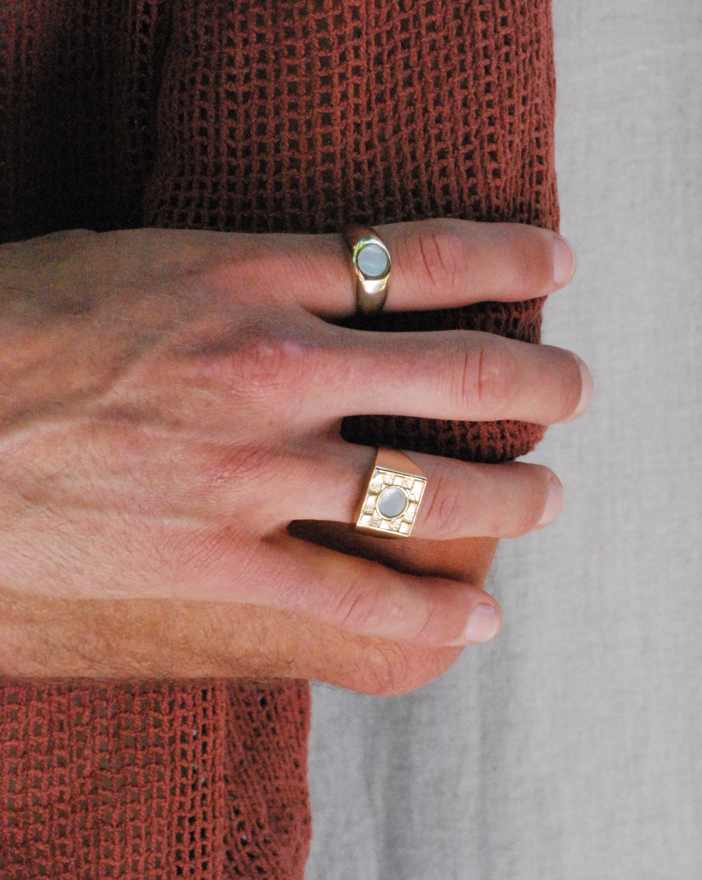 Close-up of a hand wearing two gold colored rings with white mother of pearl on a neutral background