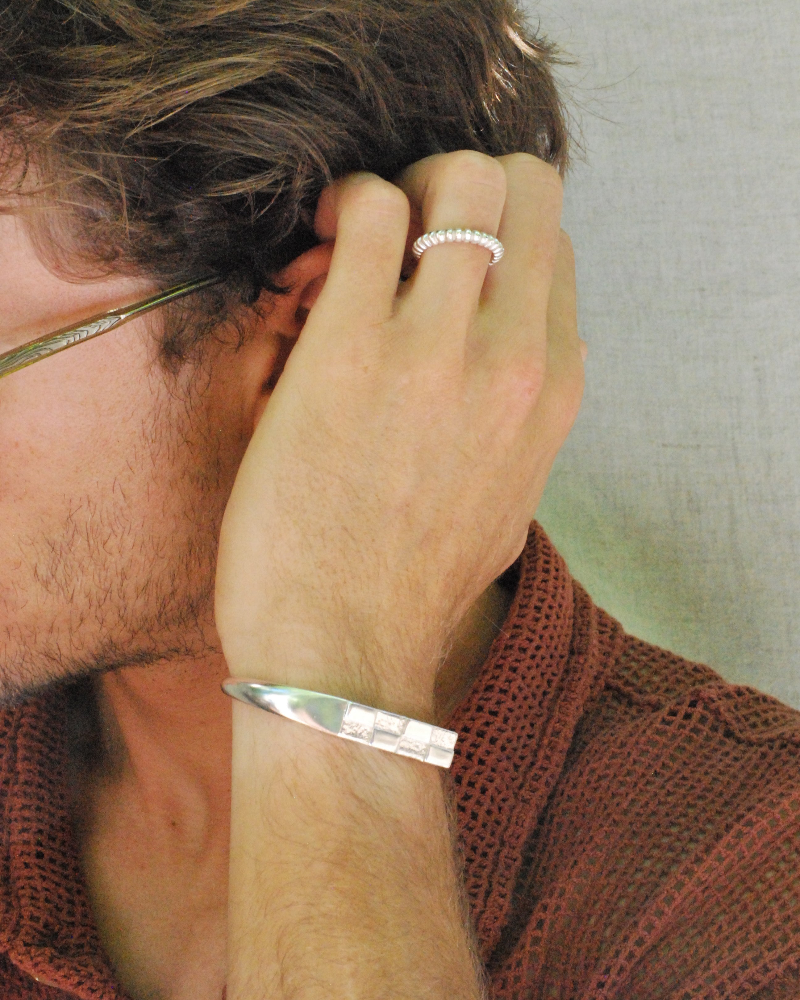 Close-up of a person with a silver bracelet and ring on a neutral background