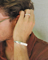 Close-up of a person with a silver bracelet and ring on a neutral background