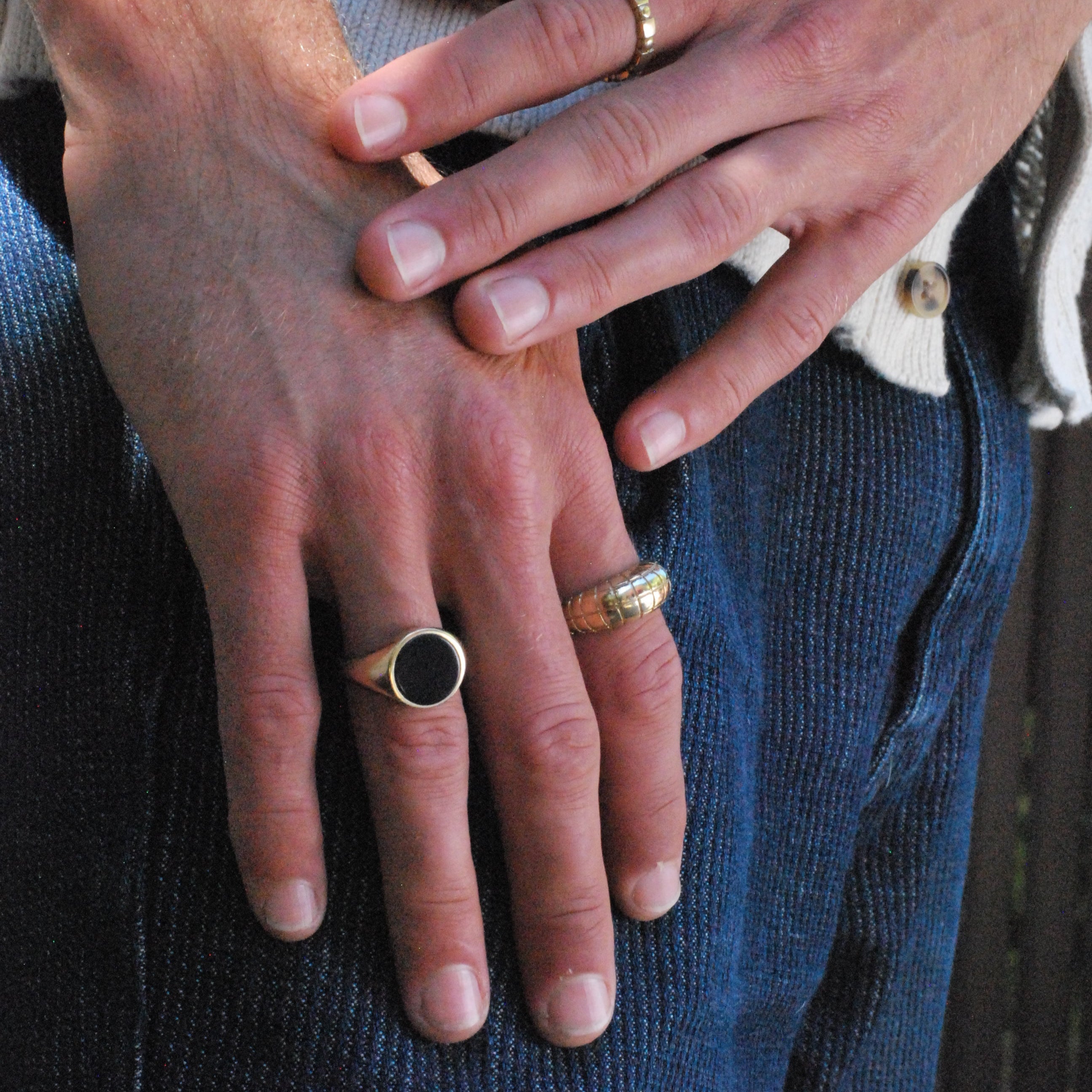 Close-up of two hands with rings on fingers including a gold toned round signet with a black onyx inlay