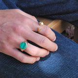 Close-up of a hand wearing two rings, one round signet with green malachite inlay on a blue denim background