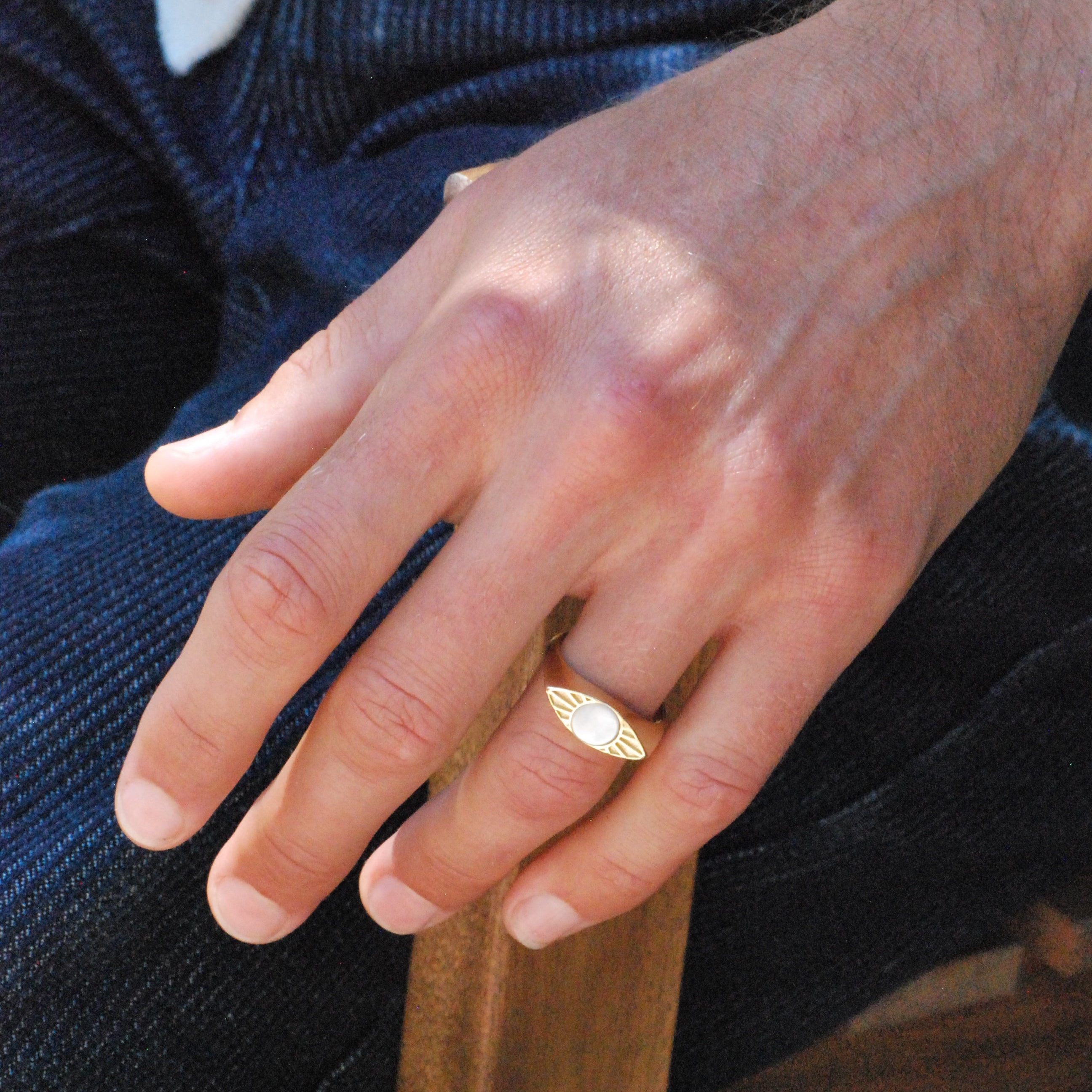 A person wearing a gold eye shaped signet ring with white mother of pearl stone inlay