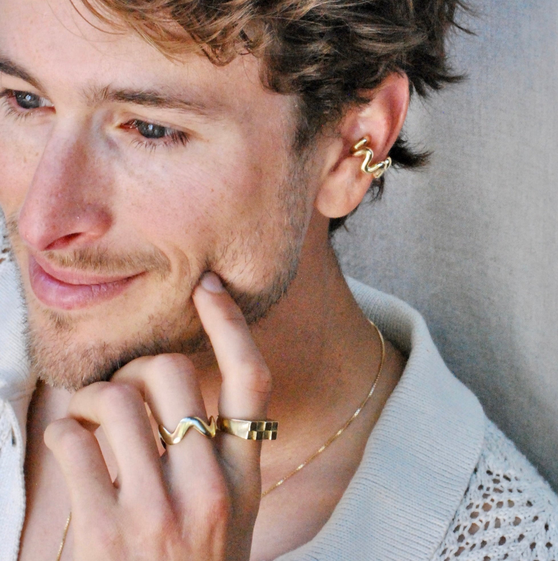 Man with styled gold jewelry against a neutral background