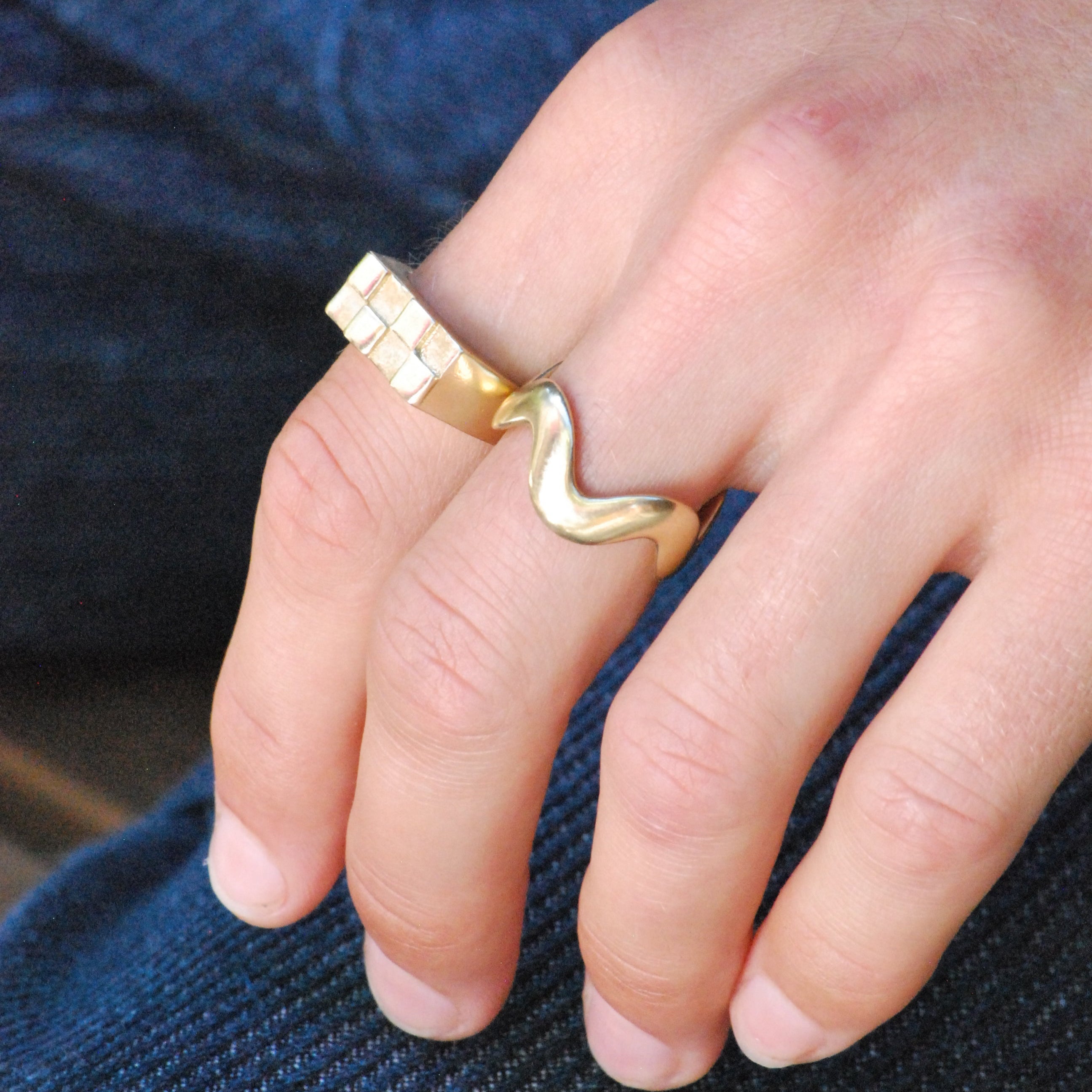 Gold ring in a wavy pattern and a checkerboard signet on a person's finger against a blue fabric background