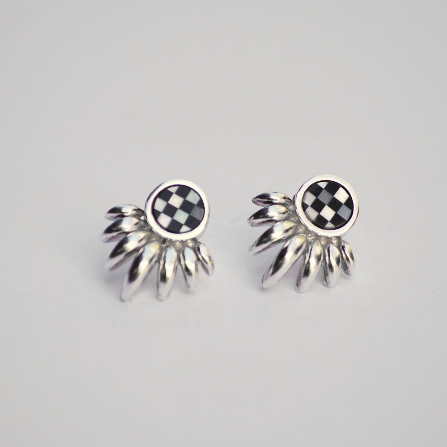 Pair of silver ray earrings with checkered inlay stone on a gray background