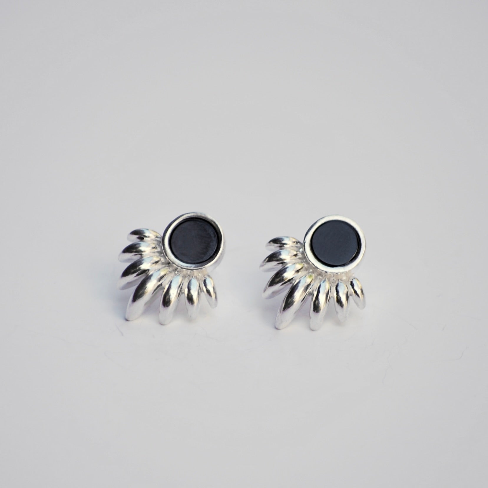 Silver sunray shaped earrings with black onyx stones on a light gray background