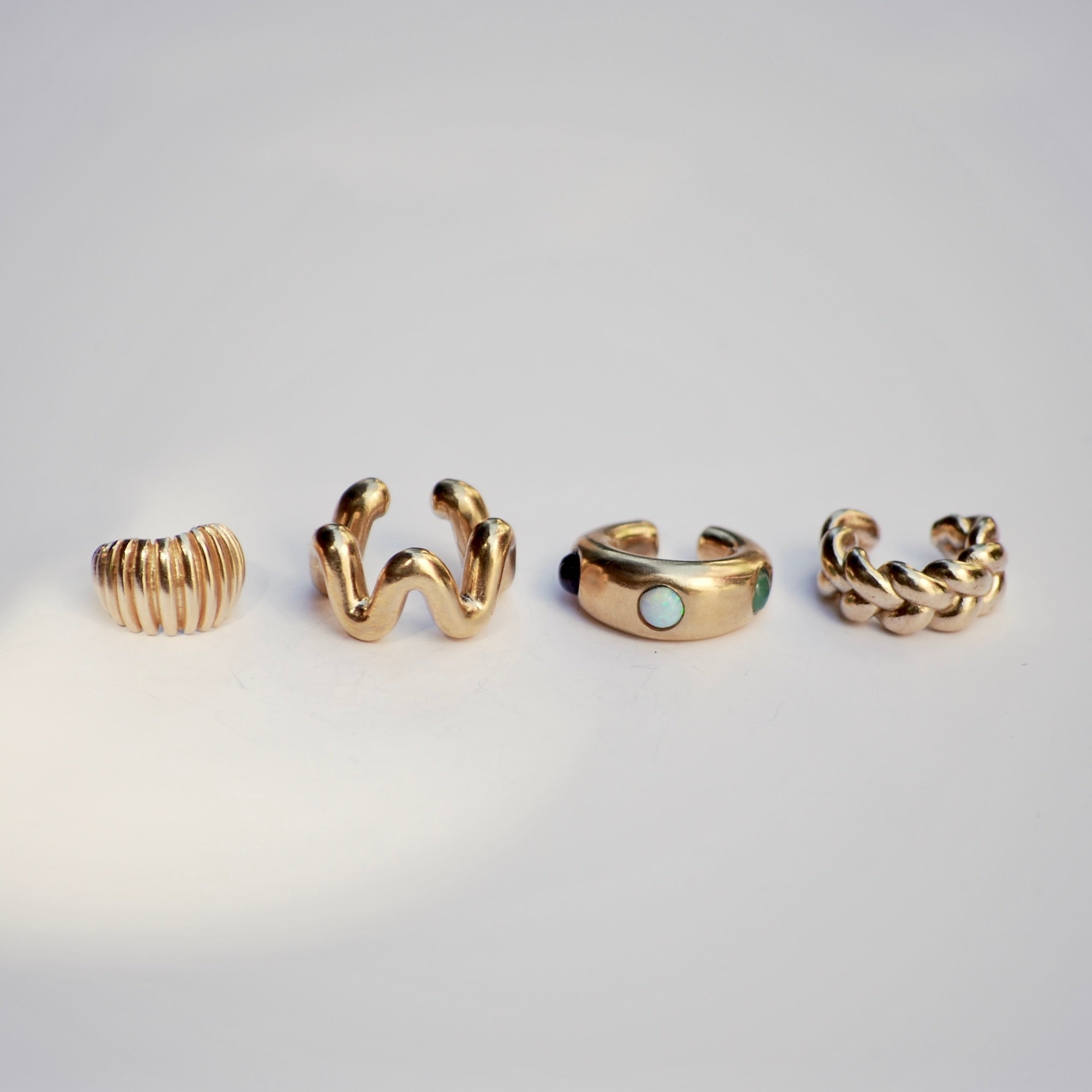 Four gold ear cuffs with different designs on a light gray background