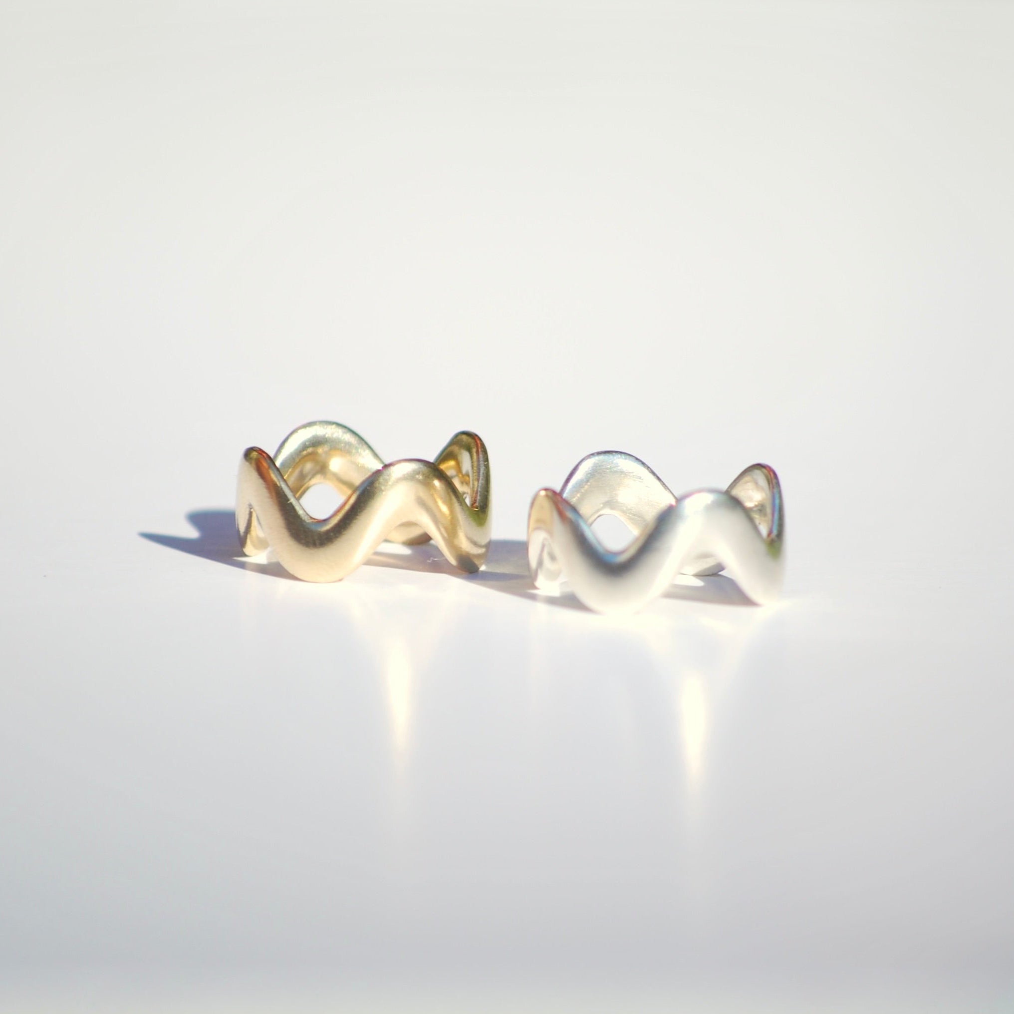 Pair of gold and silver squiggly rings on a light gray background