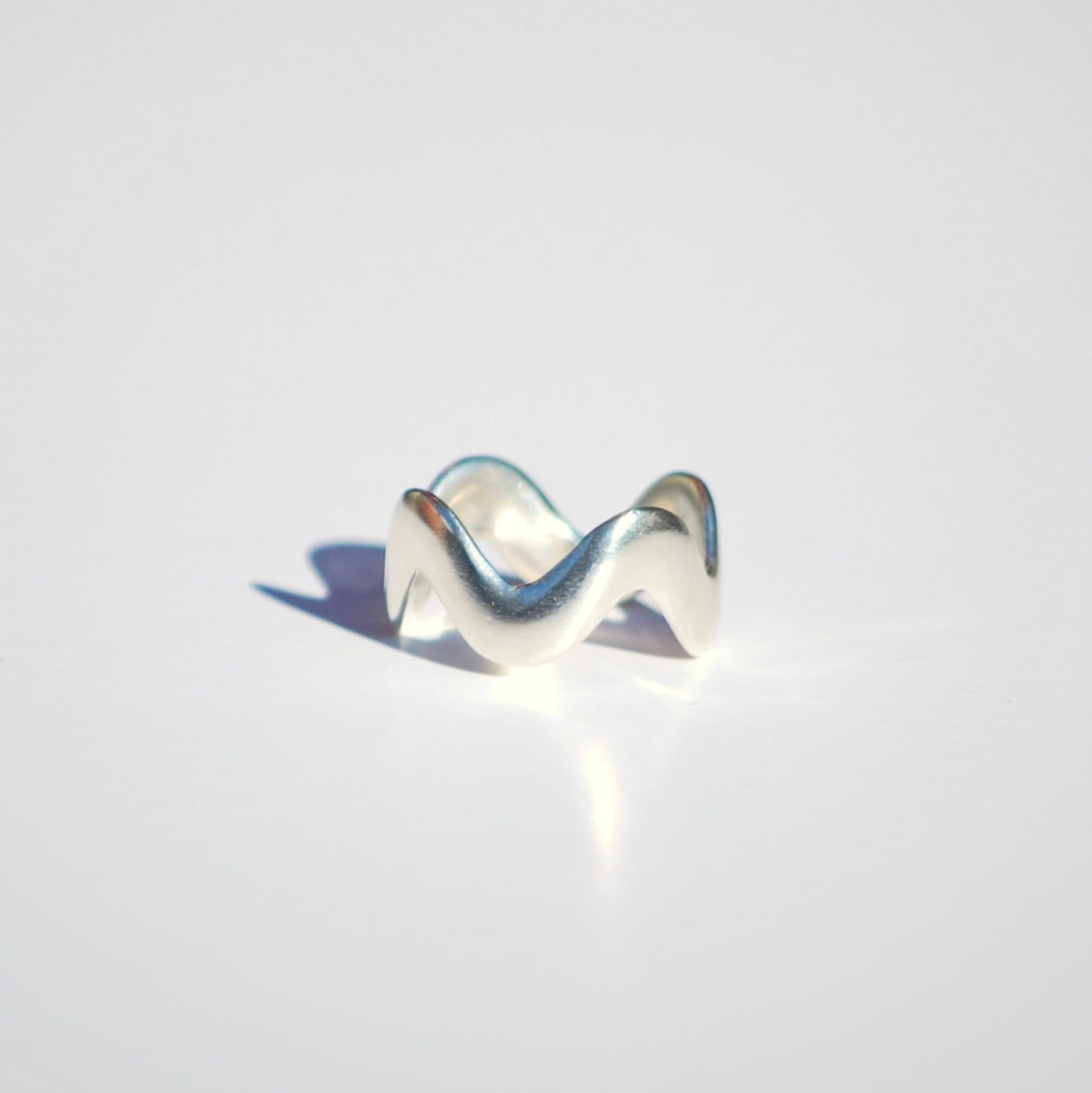 Silver ring with a wavy design on a light gray background