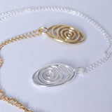 Two spiral pendants on chains, one silver and one bronze on a white background