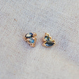 Pair of gold earrings with blue sapphire gemstones on a textured fabric background