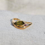 Gold ring with a green  marquis and pink round gemstone on a light gray surface