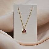 Gold necklace with a pink and orange sapphire pendant on a beige fabric background