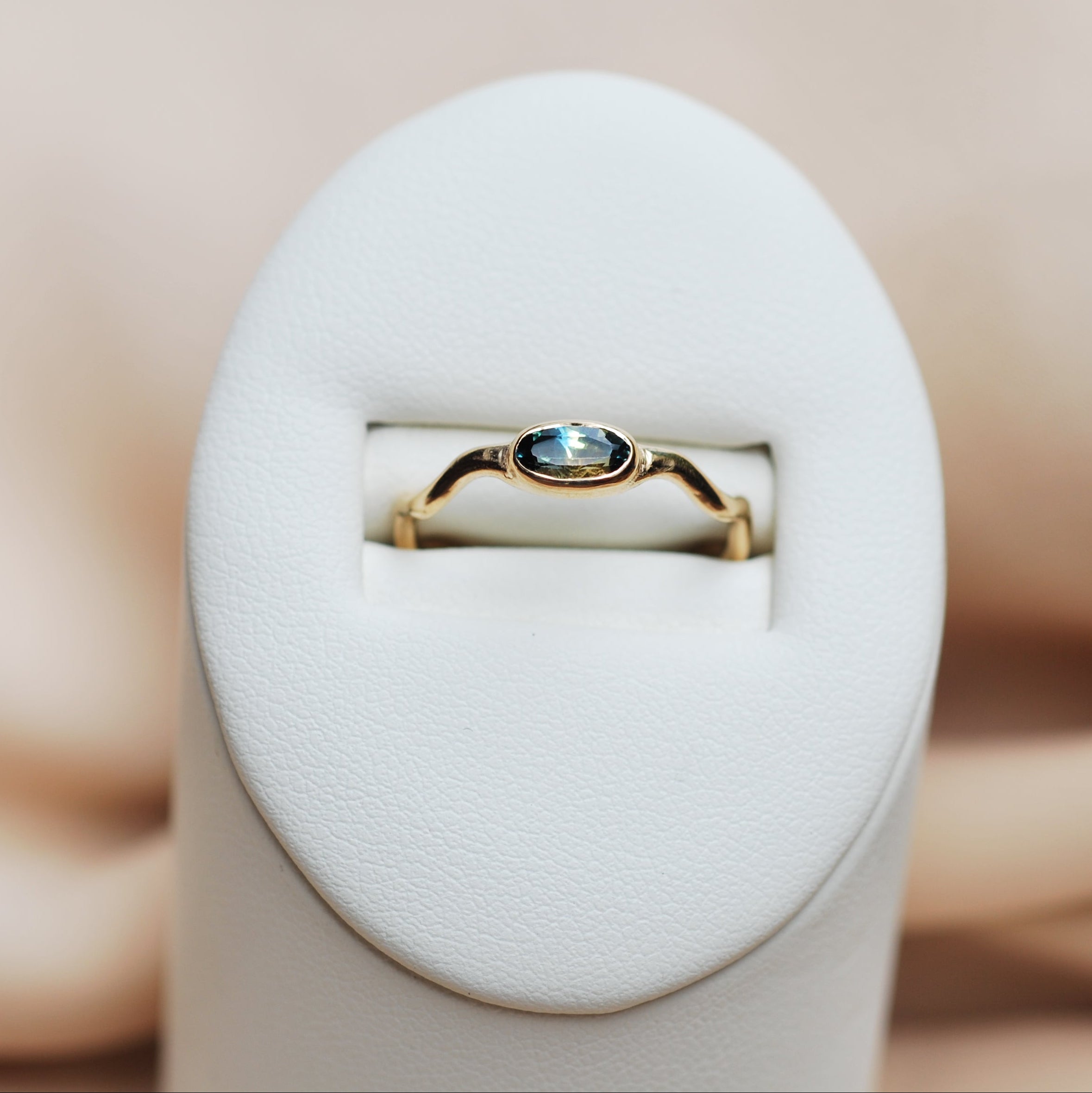 Gold ring with a blue gemstone in a white ring display on a beige background