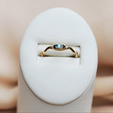 Gold ring with a blue gemstone in a white ring display on a beige background
