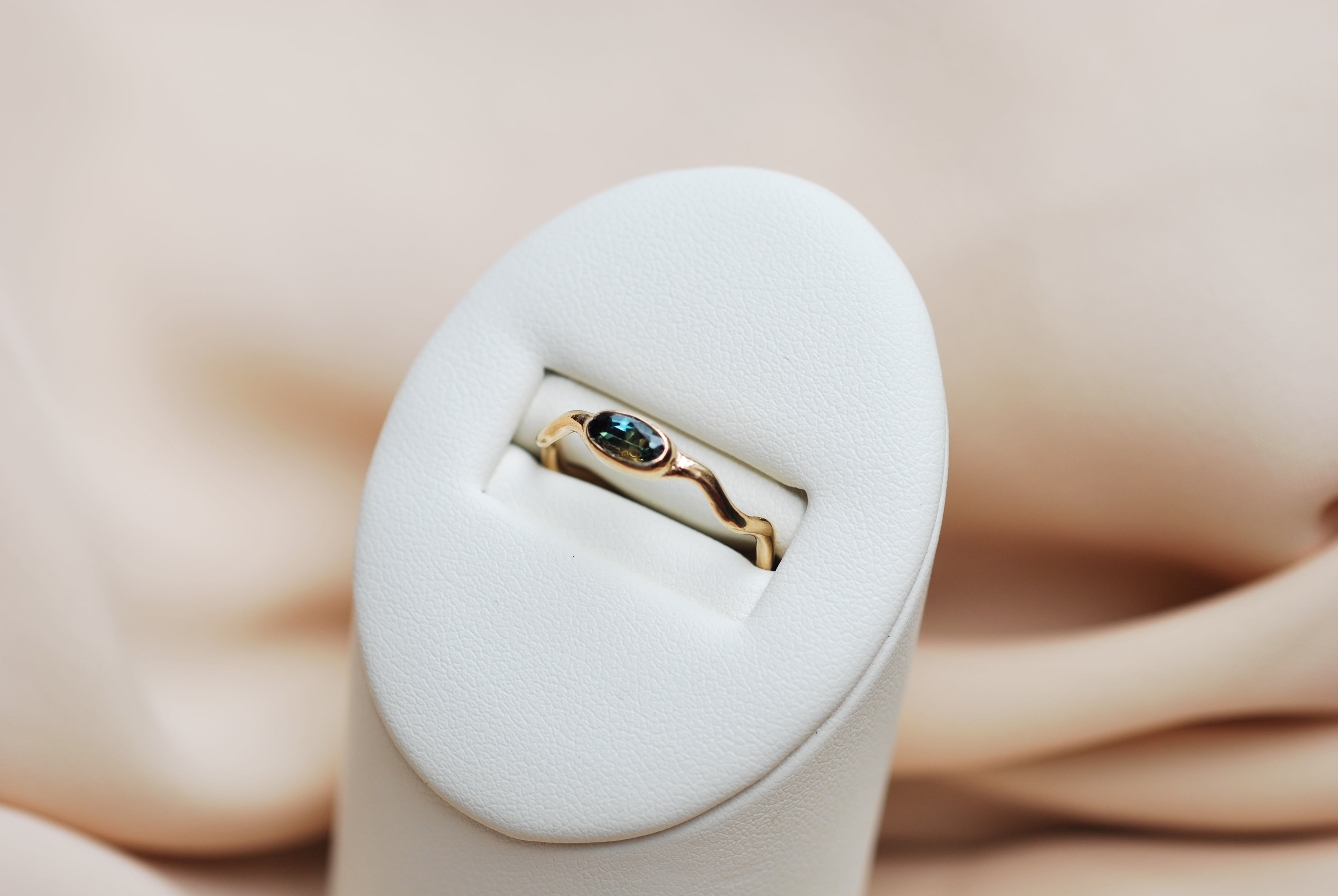 Gold ring with a blue gemstone in a white ring box on a beige background