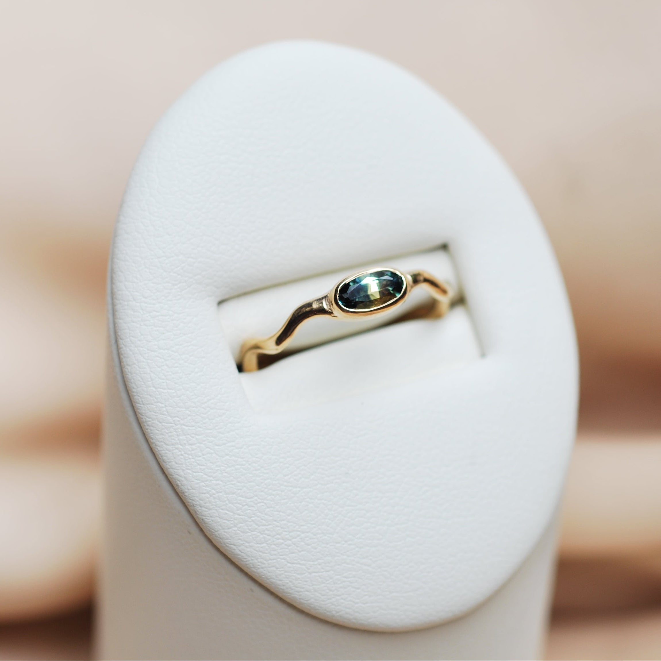 Gold ring with a bi-color sapphire gemstone in a white ring display on a beige background