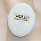 Gold ring with blue and orange gemstones on a white surface